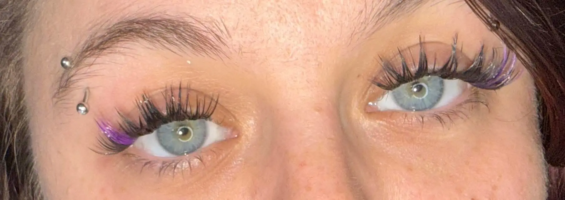 Both eyes with purple accent cluster lashes and eyebrow piercing